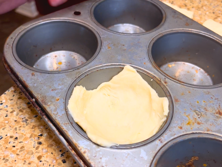 A square of puff pastry dough in a muffin tin.