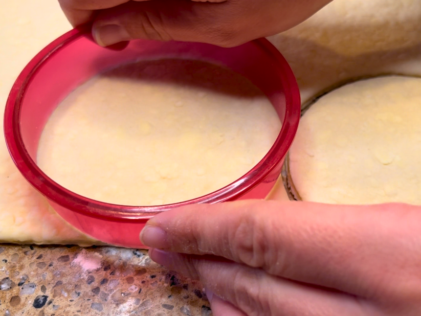 Woman cutting circles, with a cookie cutter, of puff pastry dough.