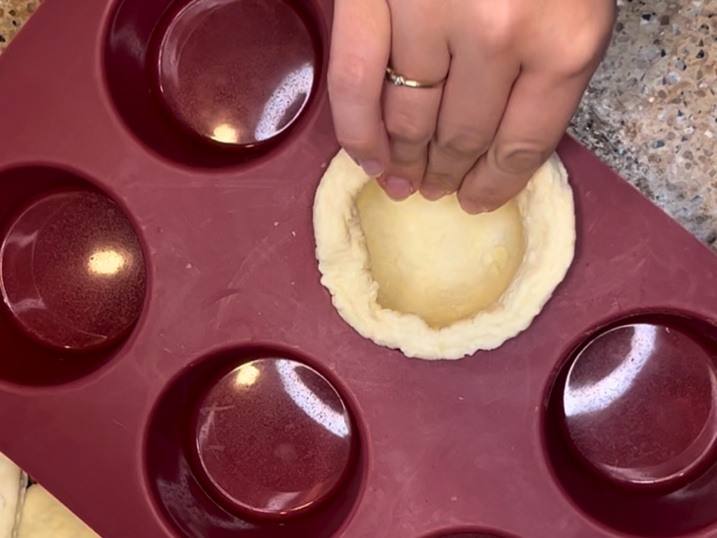 Woman pressing a circle of puff pastry into a muffin cup.