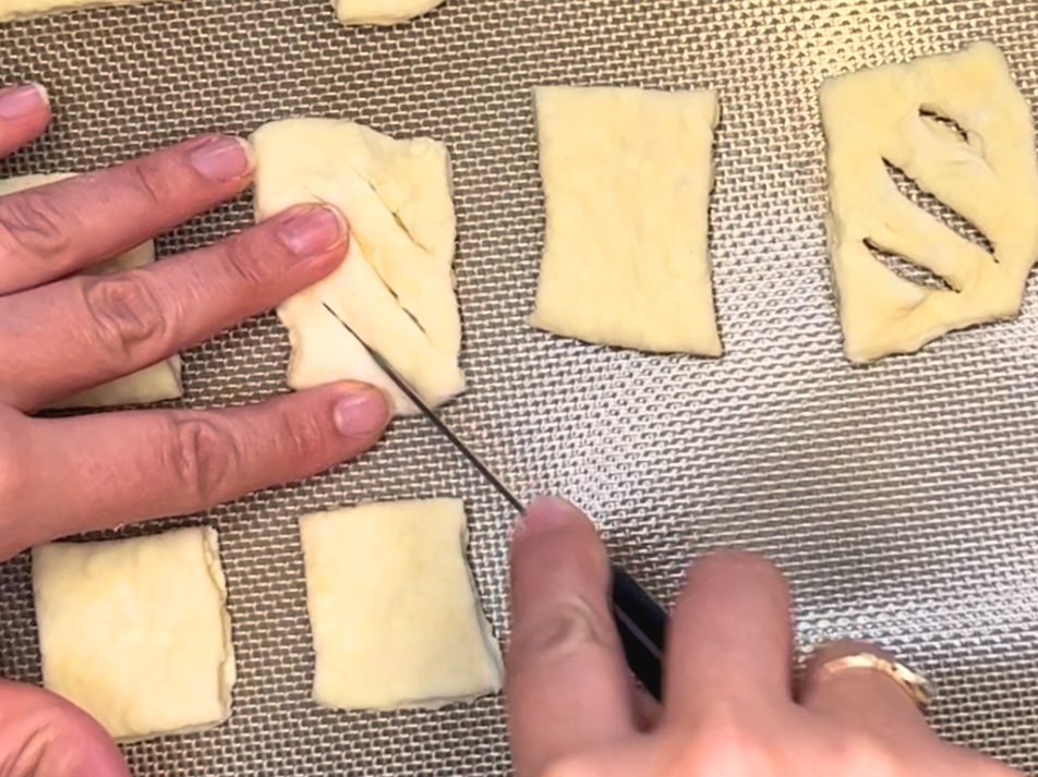 A woman cutting diagonal slashes in puff pastry dough