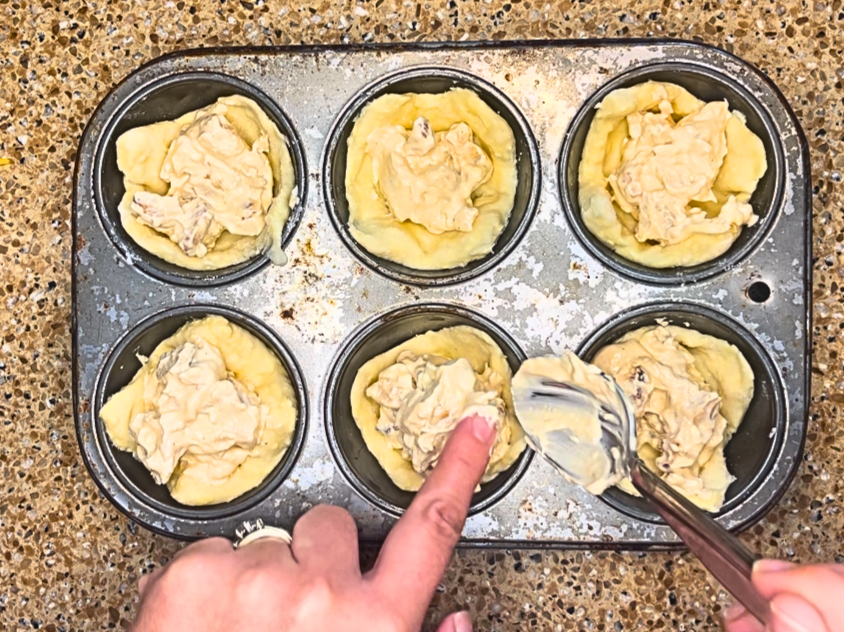 A woman placing a spicy chicken and cheese mixture into a muffin tin lined with puff pastry.