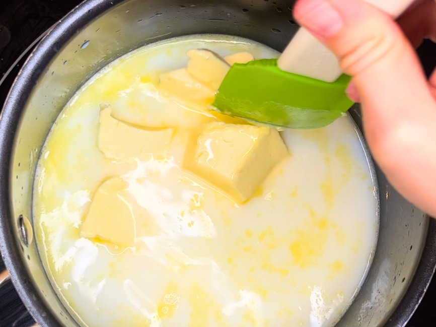 Woman stirring and melting butter into a sauce pot with milk, sugar, and water.