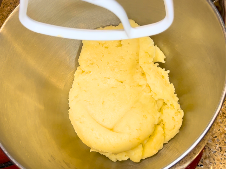 A pastry dough ball in the bottom of a bowl with a paddle attachment.