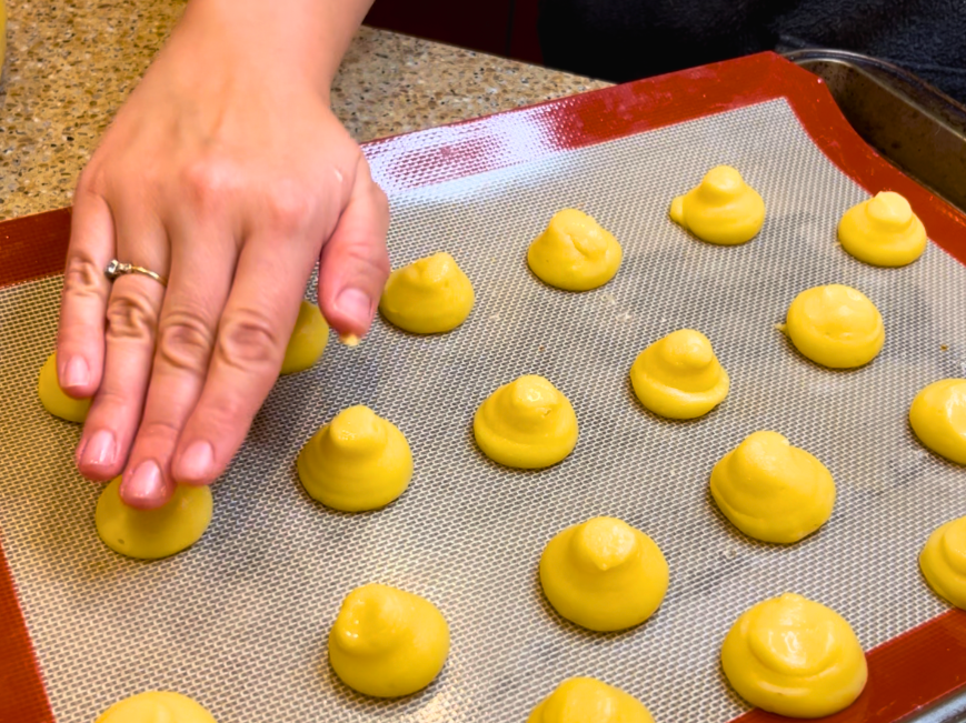 Woman pressing down the pointed tips of the pastry dough to make smooth profiteroles