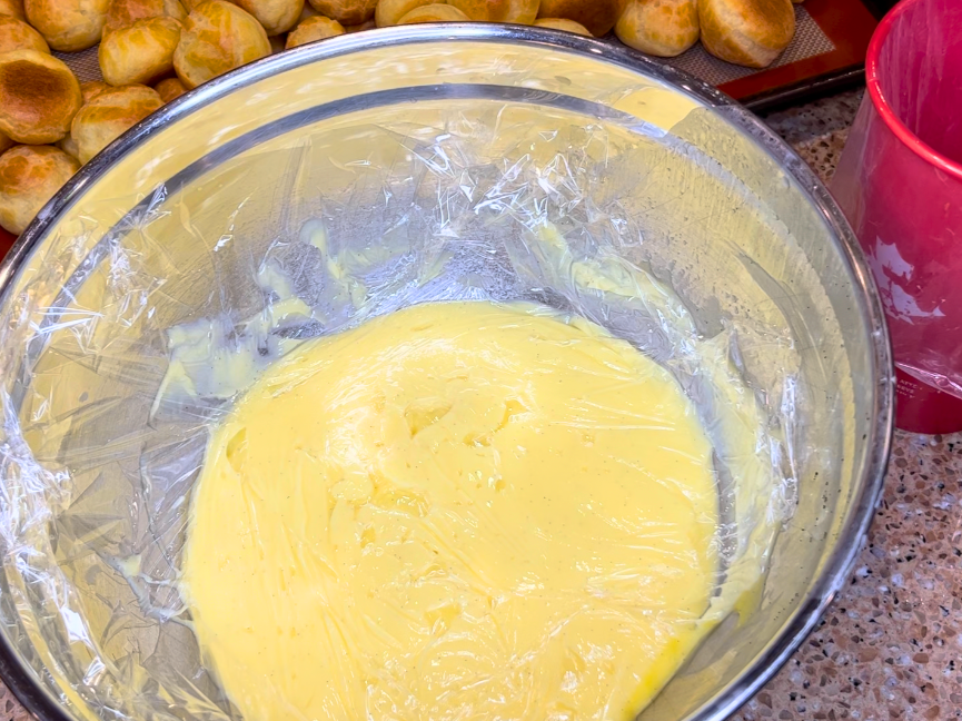A large bowl with pastry cream in it. There is a piece of cling-film resting on top.