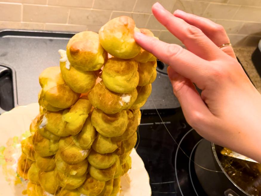 Woman placing a profiterole on the very top of a croquembouche.