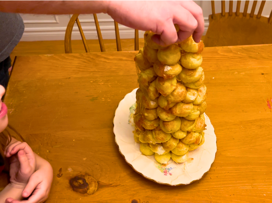 A man removing a profiterole from a croquembouche.