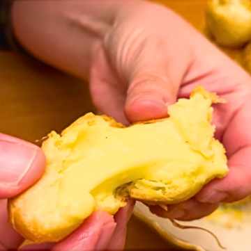 Woman showing the inside of a profiterole filled with pastry cream.