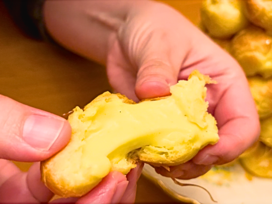 Woman showing the inside of a profiterole filled with pastry cream.
