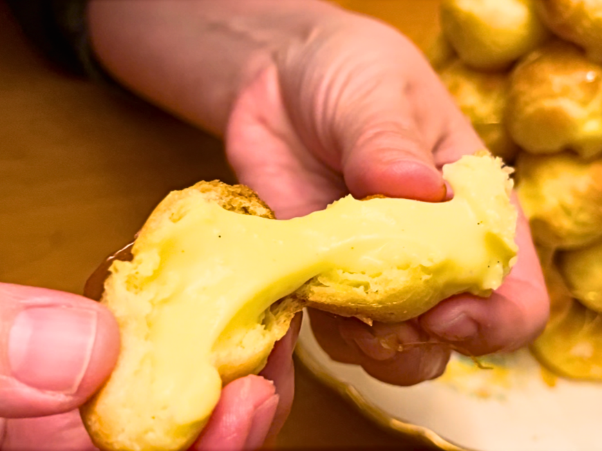 Woman showing the pastry cream inside of a profiterole.