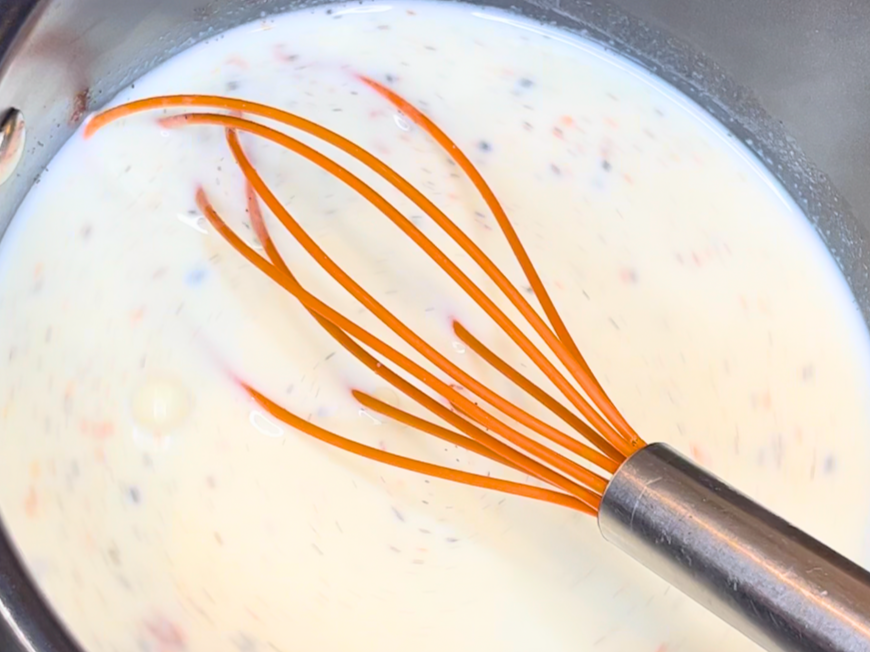 An orange whisk in a pot of milk with vanilla.