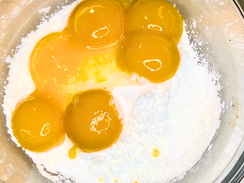Egg yolks sitting on top of sugar and cornstarch in a metal bowl.