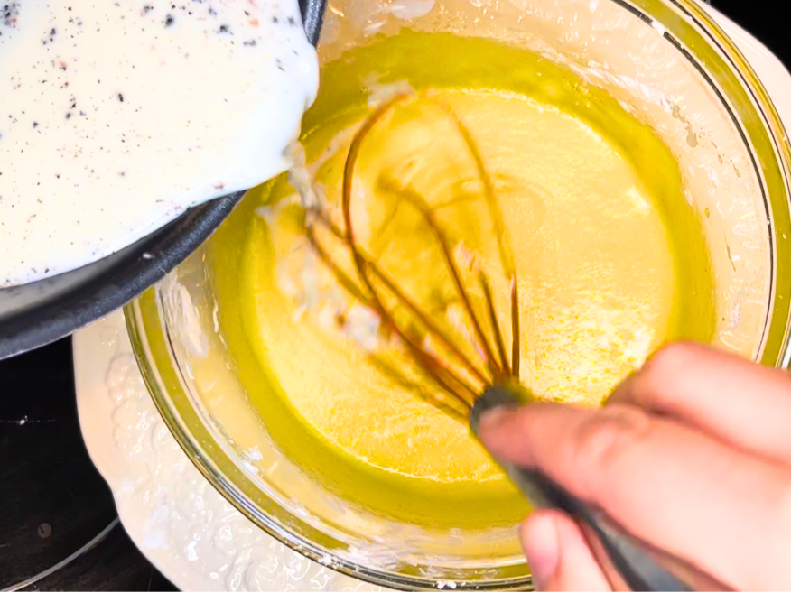 Woman pouring a hot vanilla milk mixture into a bowl with an egg yolk mixture. 