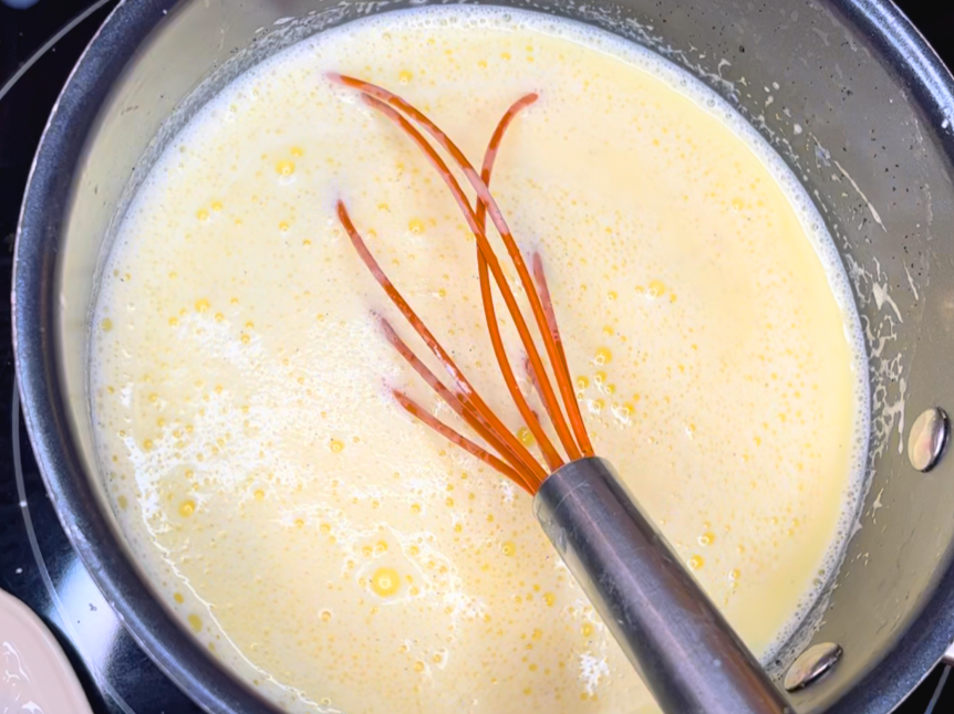 The tempered milk and egg mixture is now transferred into a sauce pot on the stove. There is a whisk inside the pot.