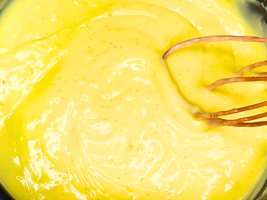A thickened pastry cream mixture in a sauce pot with a whisk in it.