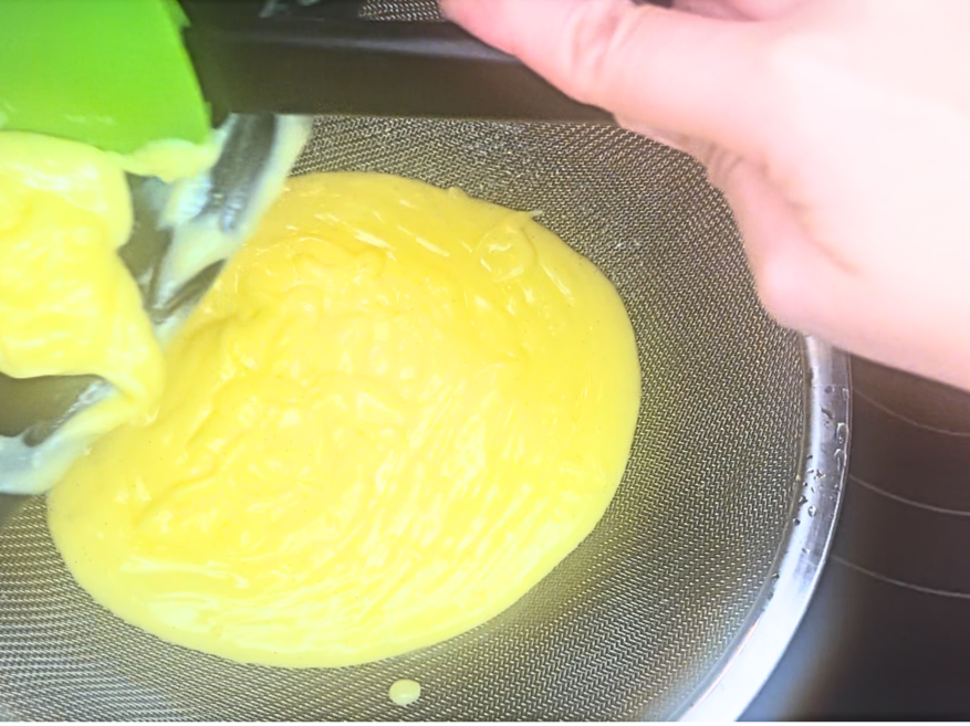 Pastry cream being poured into a fine mesh strainer.