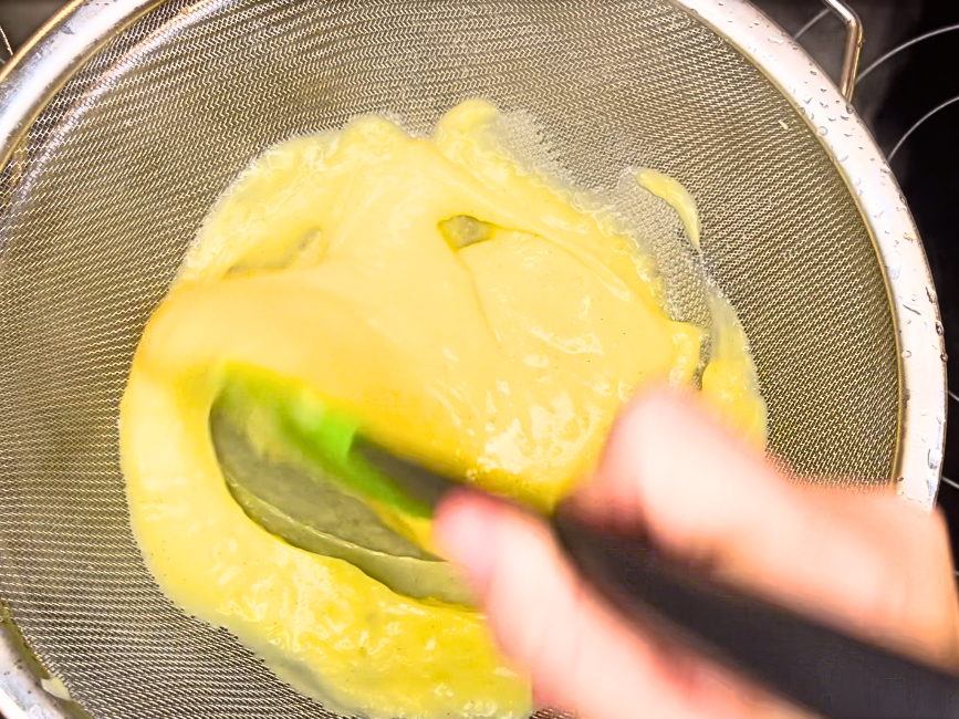 Pastry cream being passed through a fine mesh strainer.