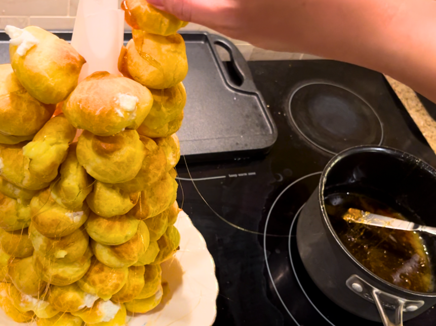 Woman placing a profiterole near the top of a tower of profiteroles stuck to a parchment paper cone.