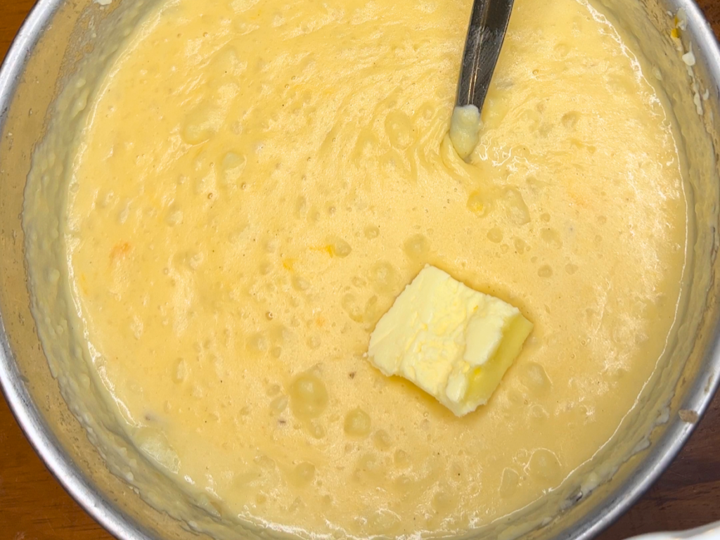 A pad of butter sitting on top of a sauce pot with potato soup in it.