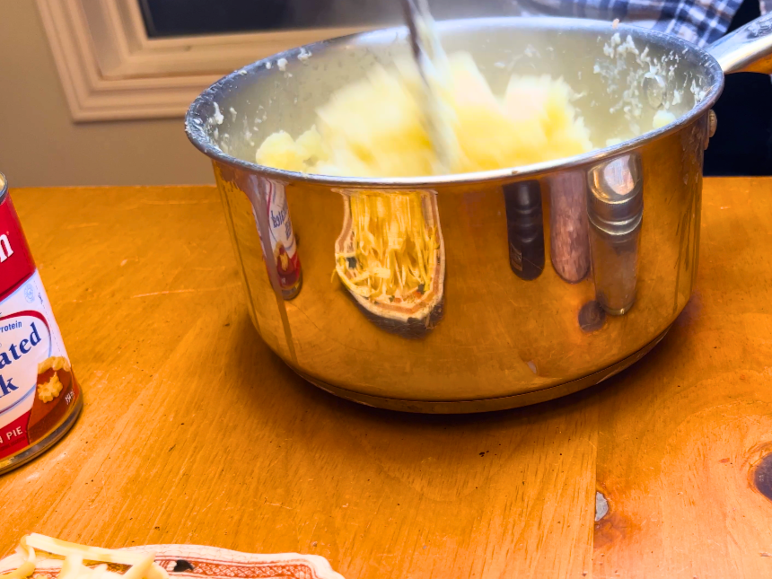 Woman mashing cooked potatoes with a potato masher, inside a metal sauce pot.