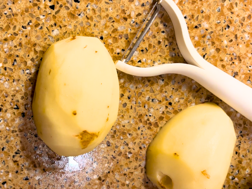 Two peeled potatoes and a white peeler beside them.