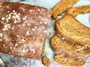 A loaf of brown bread with oats on top. There are some slices of bread cut.