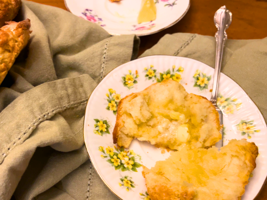 A biscuit cut in half with butter on top. It is on a yellow floral plate and has a butter knife on it.