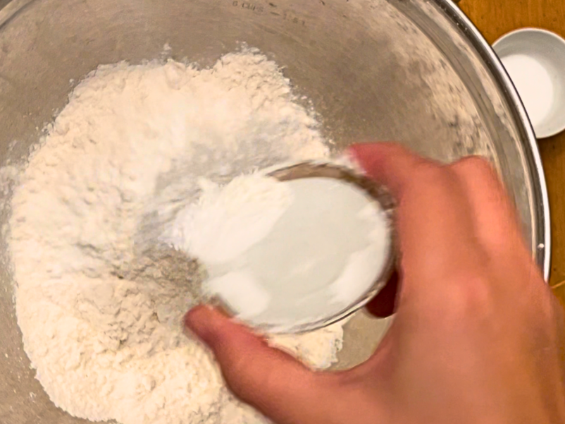 Woman adding baking powder to a bowl of flour.