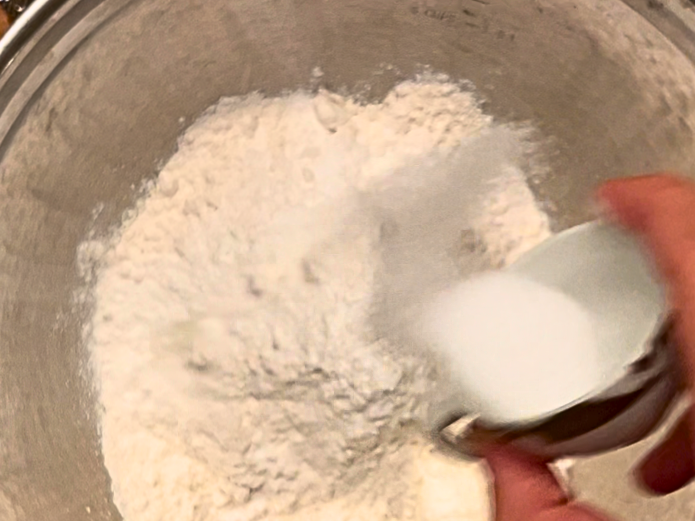 Woman adding salt to a bowl of flour.