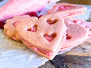 Some pink hart-shaped sugar cookies sandwiched with pink icing. The icing bag is in the background.