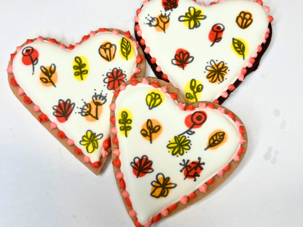 Three heart-shaped sugar cookies decorated with royal icing depicting a floral pattern.