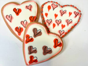 Three heart shaped decorated sugar cookies with coloured hearts on them.