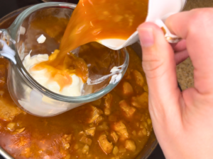 Woman tempering a cup of sour cream with liquid from the chicken paprikash