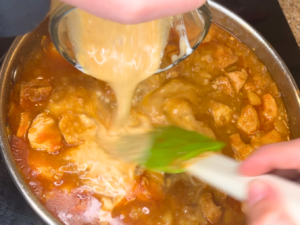 Woman pouring a mixture of sour cream and liquid from chicken paprikash back into the stew.