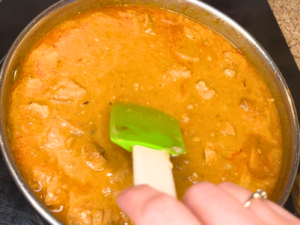 Woman stirring a pan of chicken paprikash with a green and white spatula.