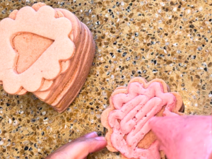 A woman piping pink icing onto strawberry sugar cookies.