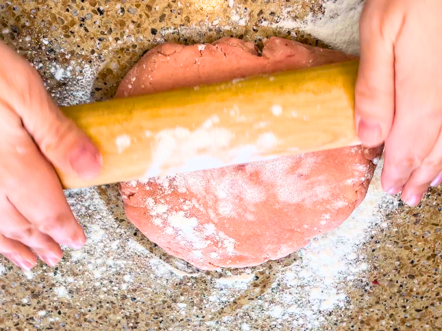 Woman rolling out pink sugar cookie dough.