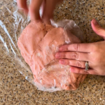Woman pressing out pink cookie dough onto a piece of cling-film.