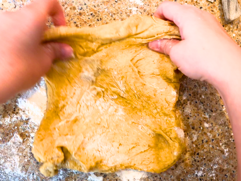 Woman folding brown bread dough.