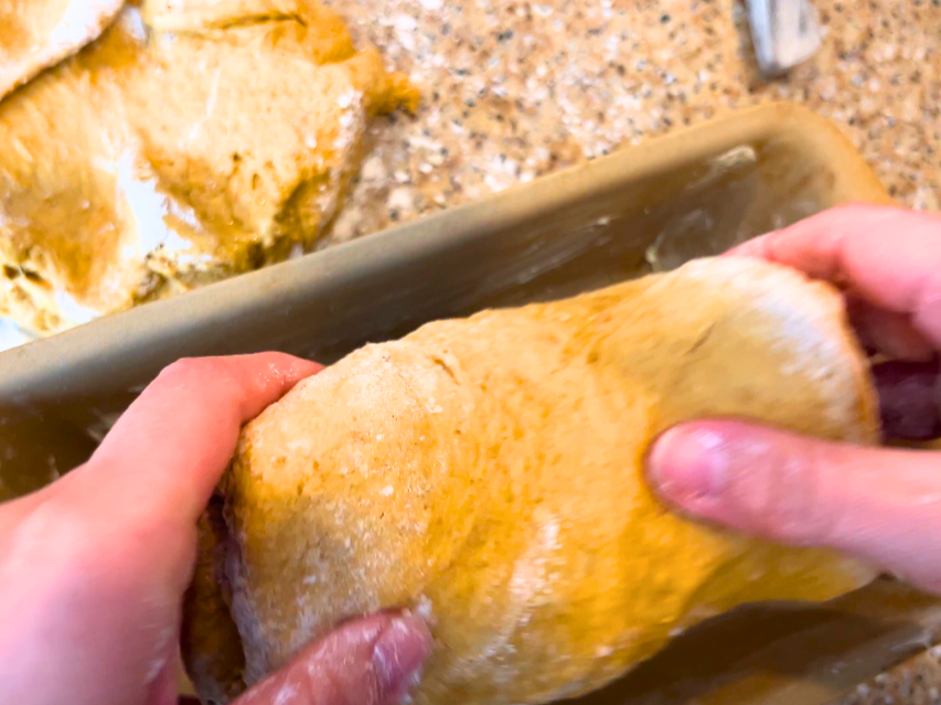 Woman placing brown bread dough into a loaf pan.