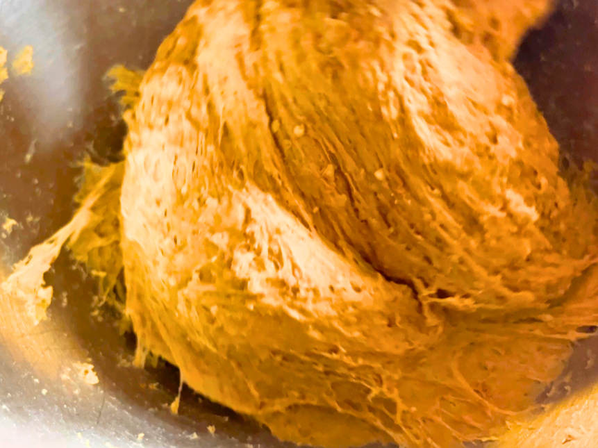 Whole wheat bread dough mixing in a stand mixer with the dough hook attachment.