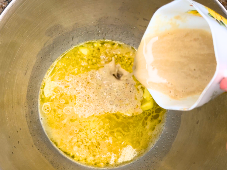 Woman pouring a cup of softened yeast into a bowl with with melted butter, water, and rolled oats.