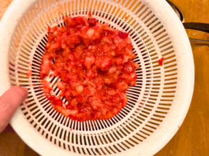 Woman holding a white strainer with mashed strawberries in it.