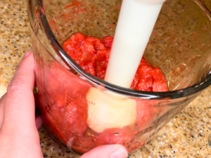 Woman using an immersion blender to puree mashed strawberries, in a large glass measuring cup.