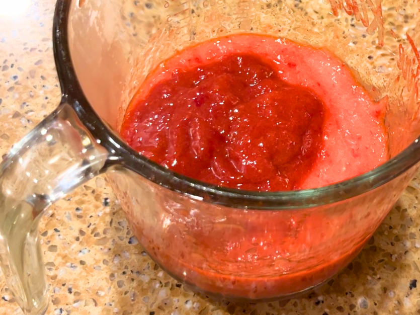 A glass measuring cup with pureed strawberries and darker cooked down strawberry juice inside.