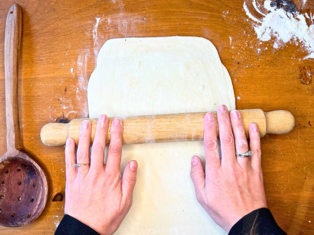 A woman is rolling out puff pastry with a wooden rolling pin.