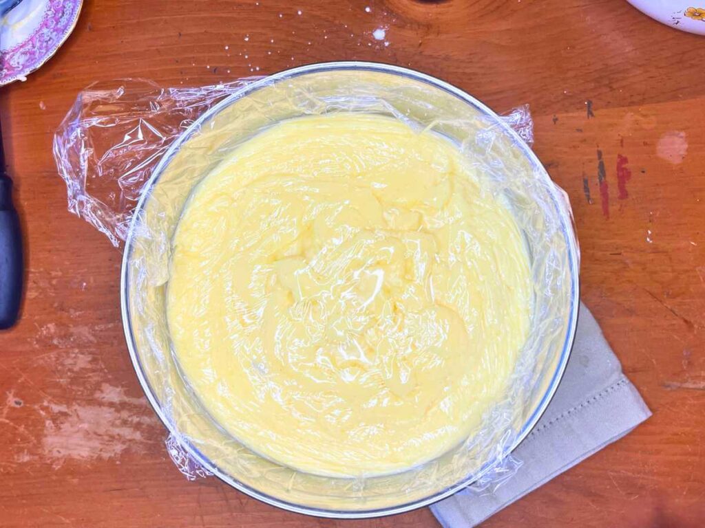 A bowl of pastry cream with plastic wrap in top.