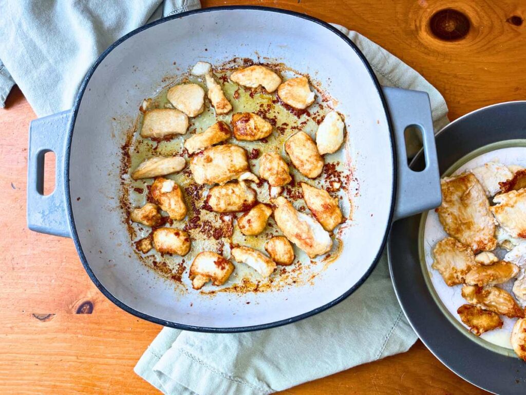 A large Dutch oven with chicken pieces frying inside.