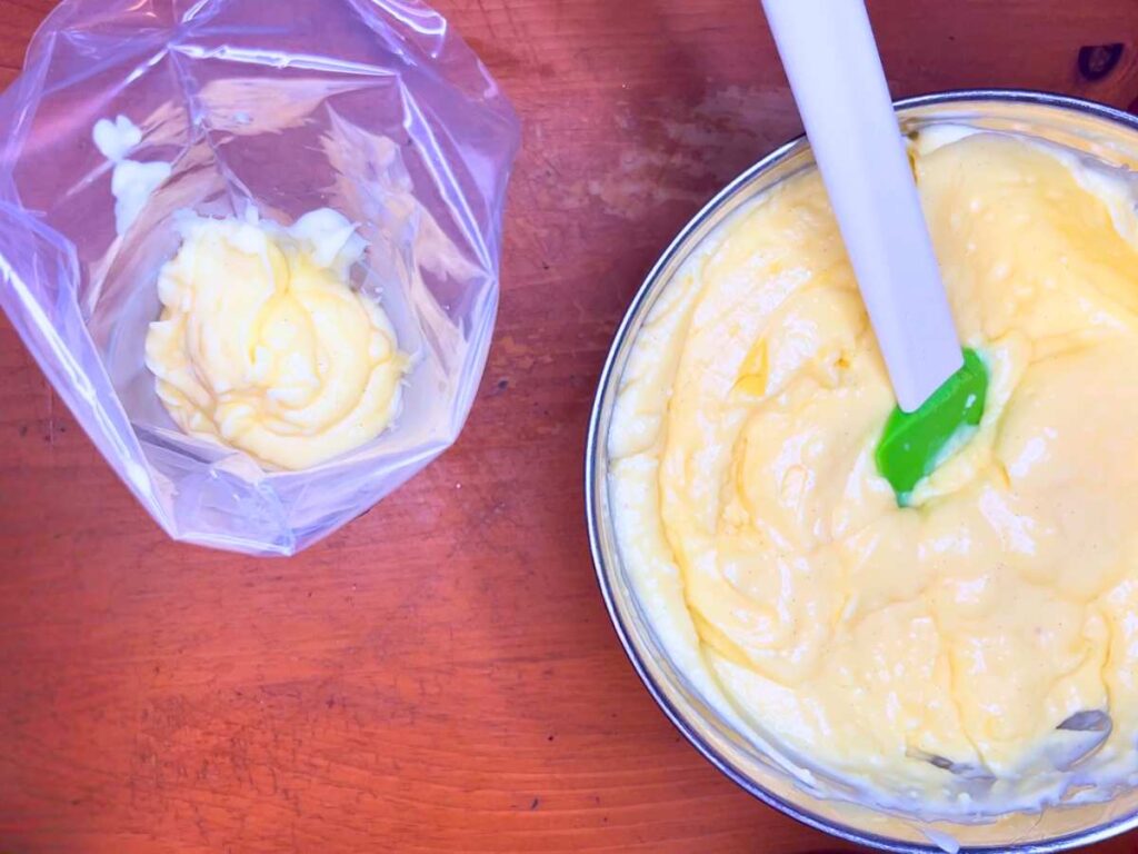 A bowl of pastry cream being scooped onto a pastry bag.