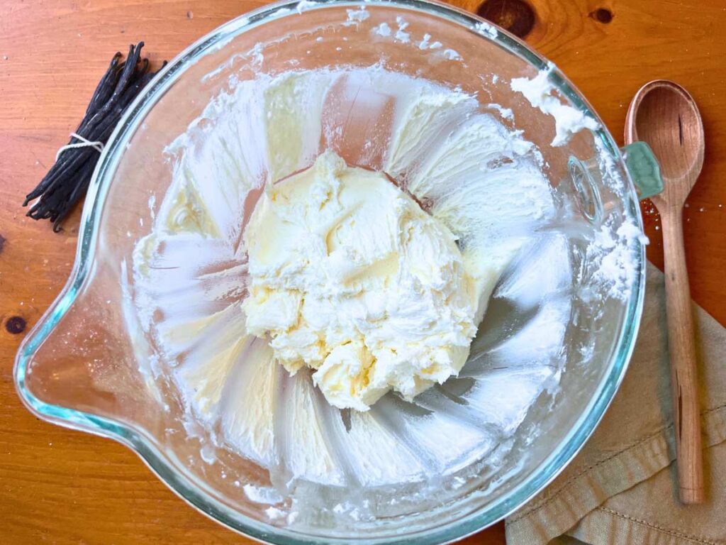 A glass bowl with creamed butter and icing sugar inside.